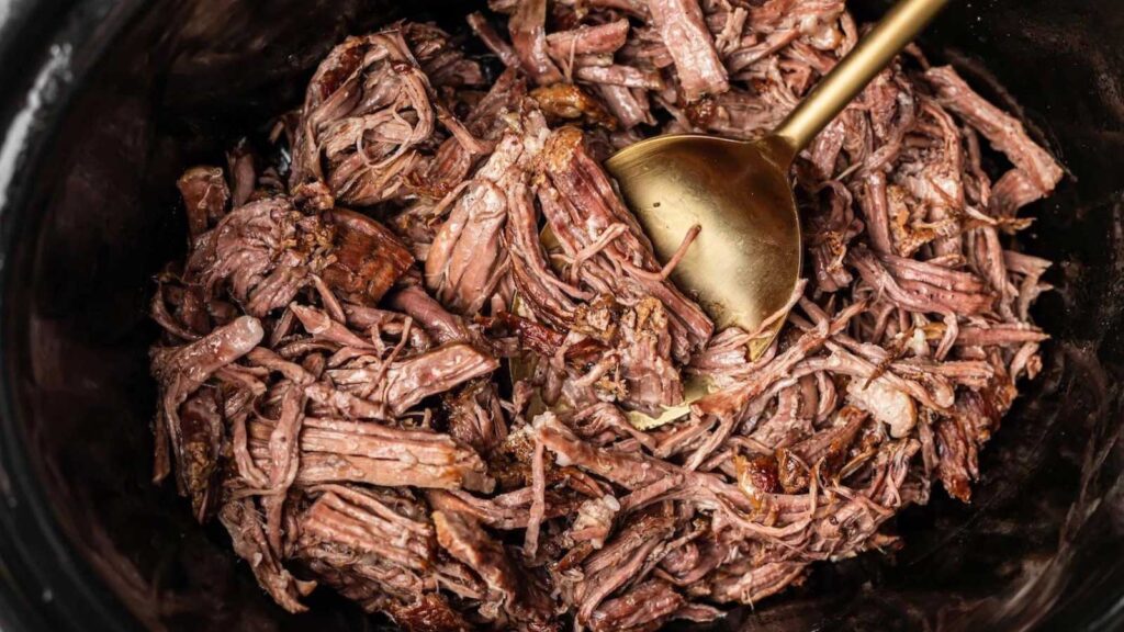An overhead view of a black crock filled with shredded beef.