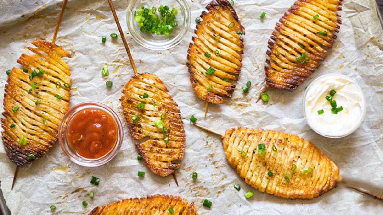 Accordion potatoes laying on parchment with small bowls of dip.