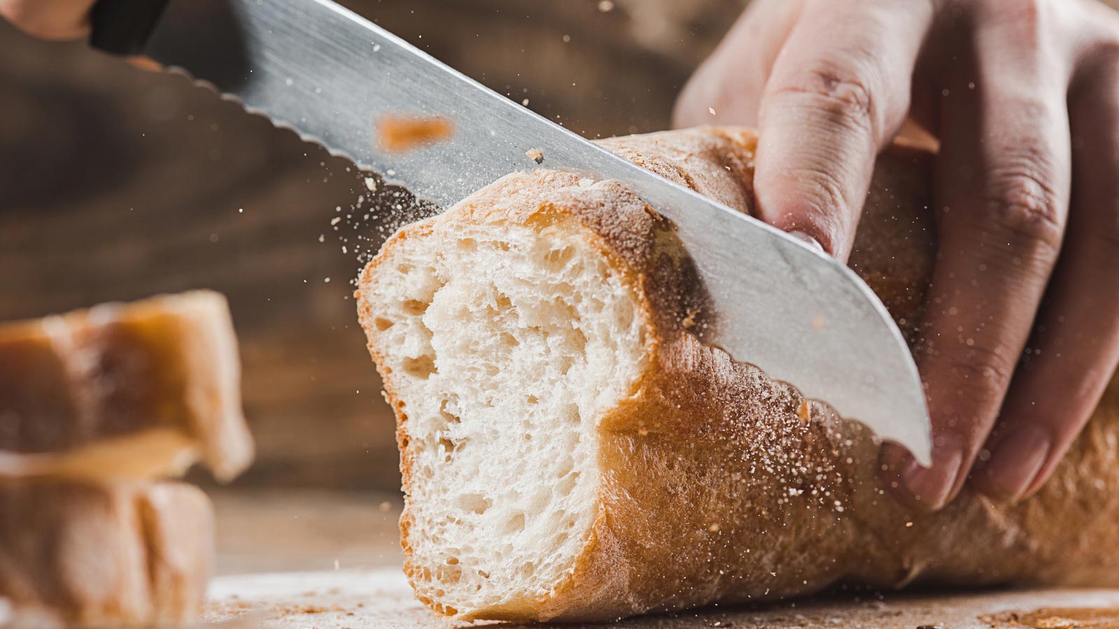 Whole grain bread put on kitchen wood plate with a person holding a knife and cutting off a slice.