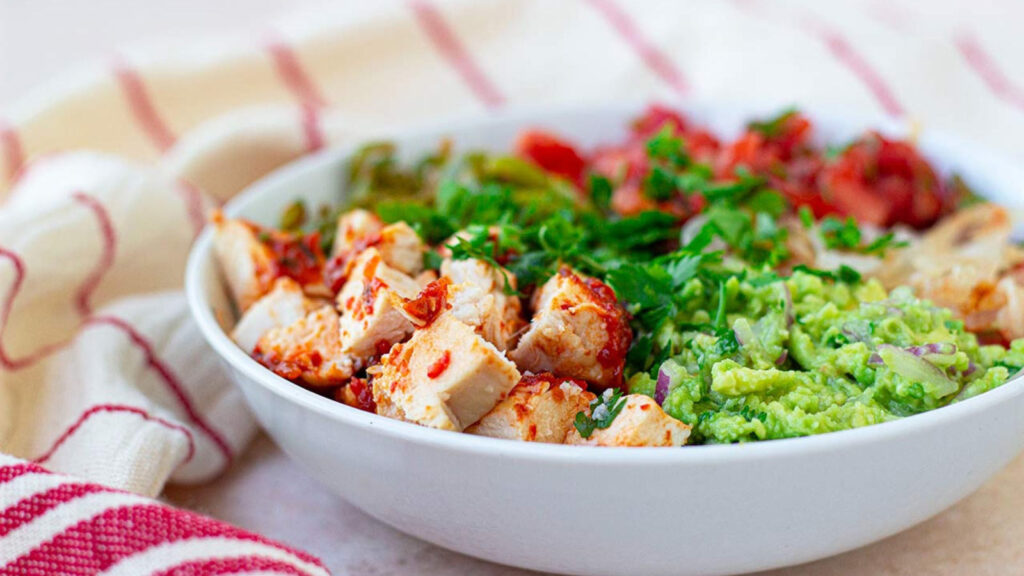 A side view of a white bowl filled with avocado chicken salad.