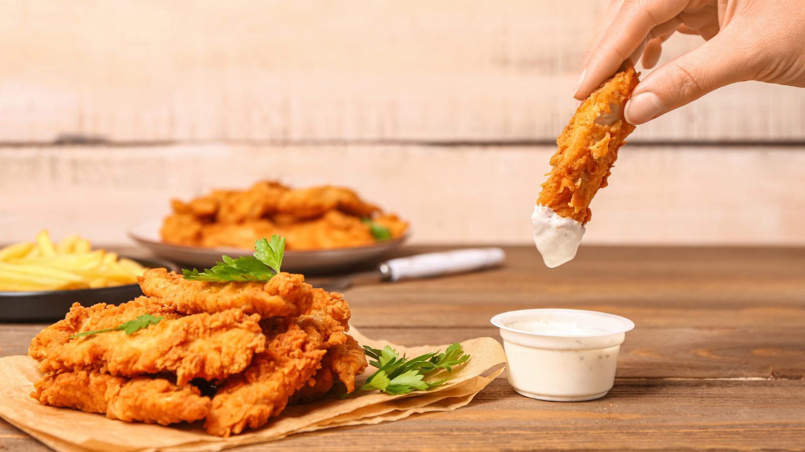 Woman dipping tasty nugget into sauce on wooden table.