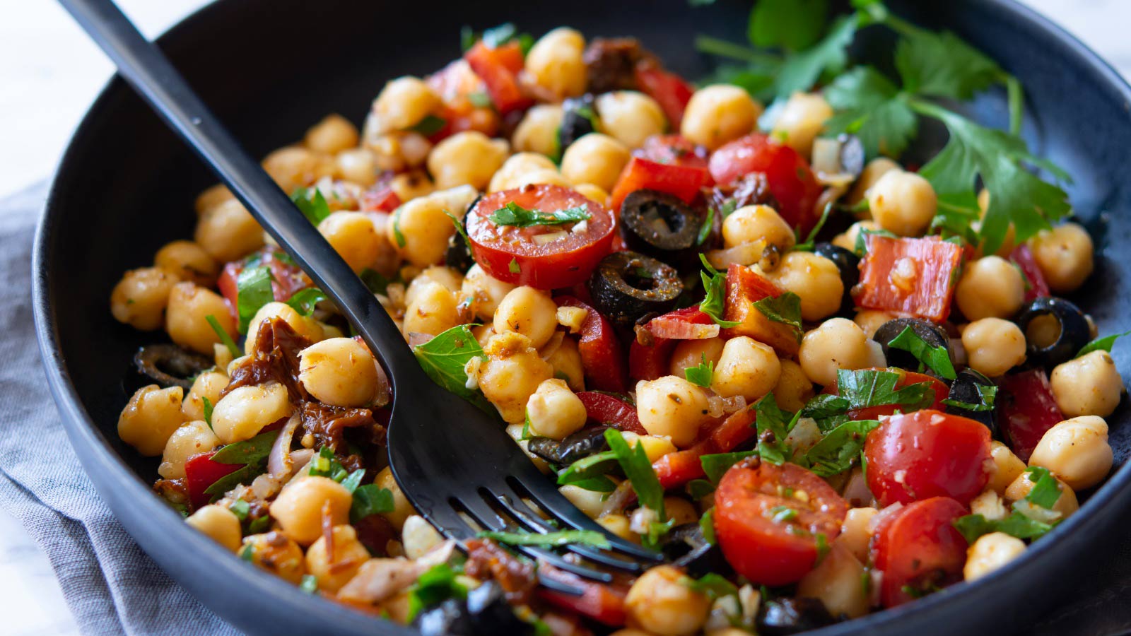 Fit and healthy beautifully colorful vegetarian chickpea salad with pepper, black olives and tomatoes. Served in a dark plate.