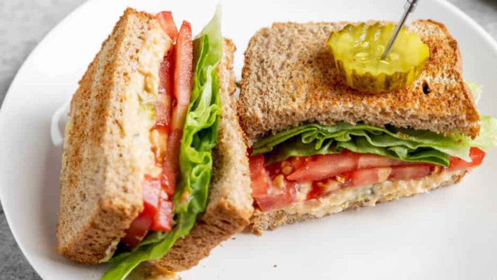 A chickpea salad sandwich cut in half on a white plate.