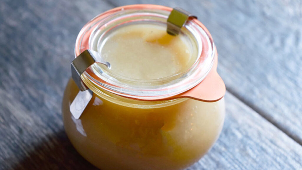 A closed and sealed jar of coconut caramel sauce on a gray surface.
