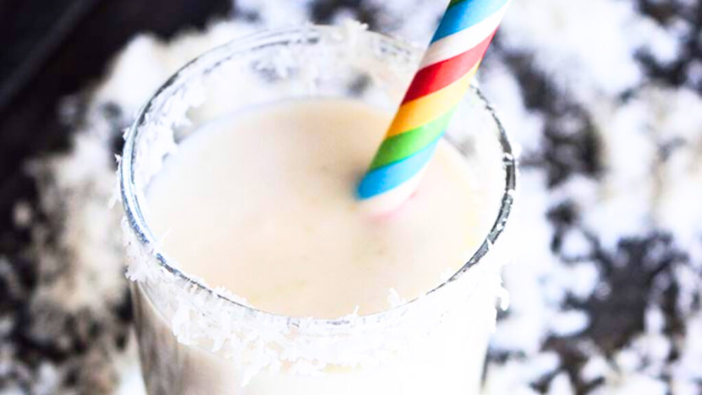 A closeup of a glass filled with coconut milk smoothie with a stripped straw and garnished with coconut shred around the rim of the glass.