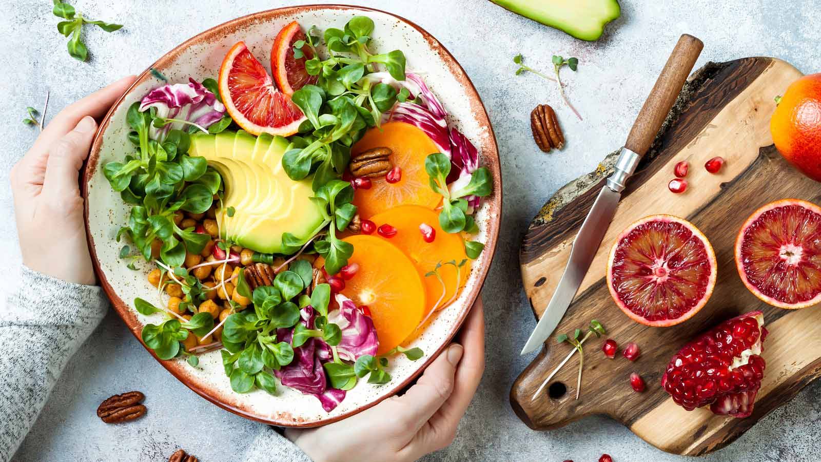 Girl holding vegan, detox Buddha bowl with turmeric roasted chickpeas, greens, avocado, persimmon, blood orange, nuts and pomegranate.