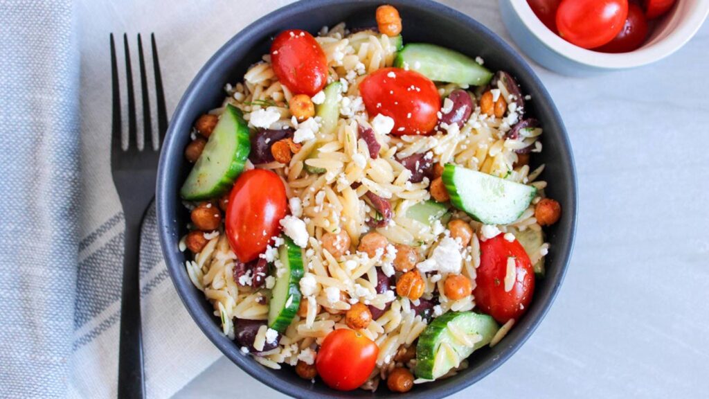 Overhead view of a black bowl filled with Greek Orzo Salad.