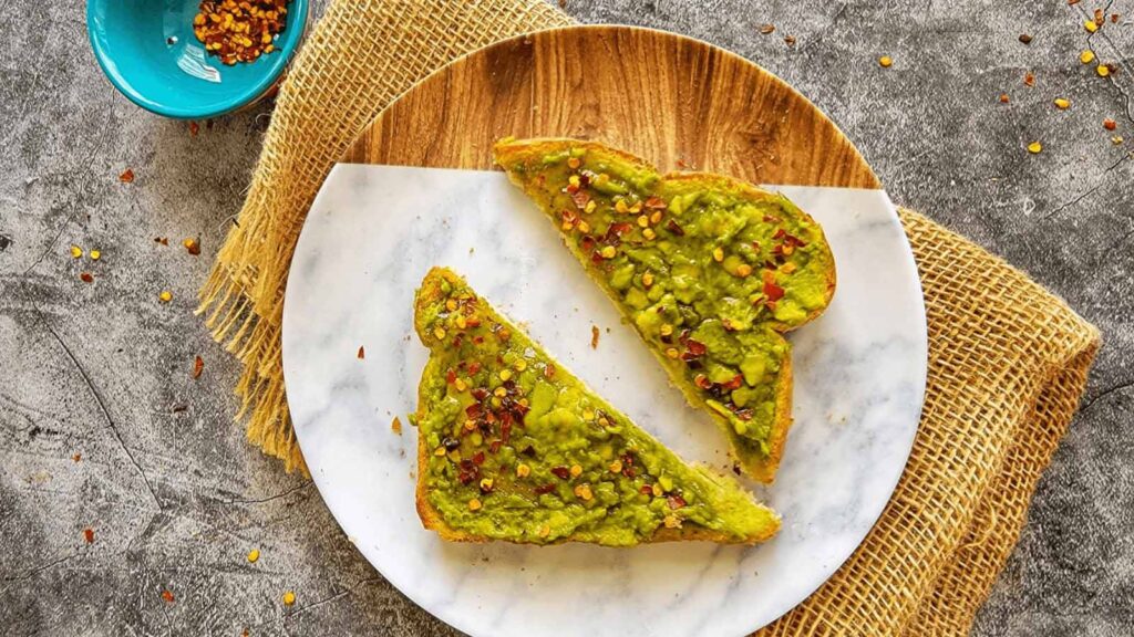 An overhead view of a wood plate holding a cut slice of honey avocado toast.