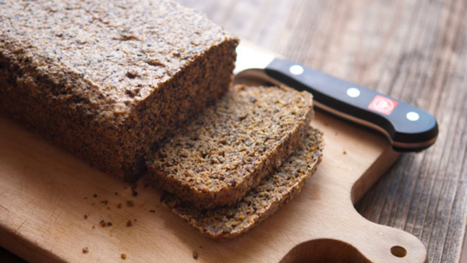A low of low carb bread on a cutting board with a bread knife. Two slices have been sliced off and lay at the front of the loaf.