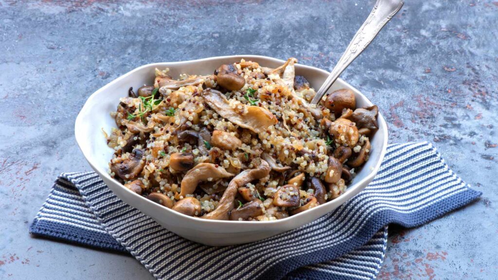A white bowl filled with mushroom quinoa on a gray surface.