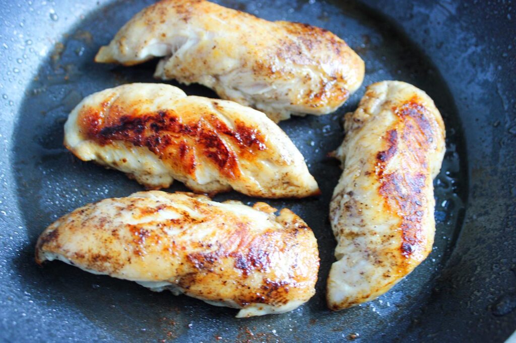 Chicken tenders cooking in a skillet.