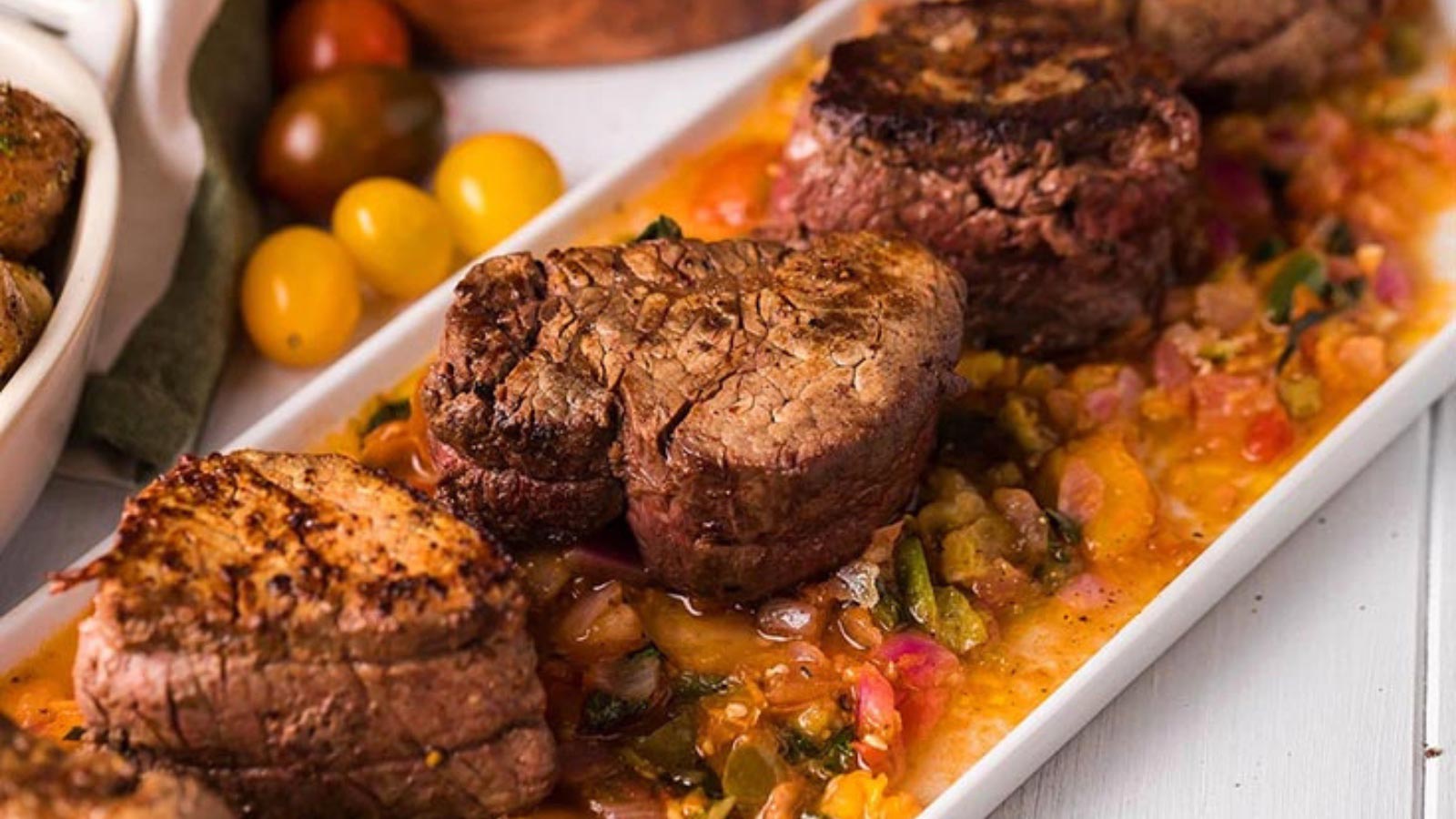 A white platter holds stacks of pan roasted beef tenderloin medallions with tomato relish.