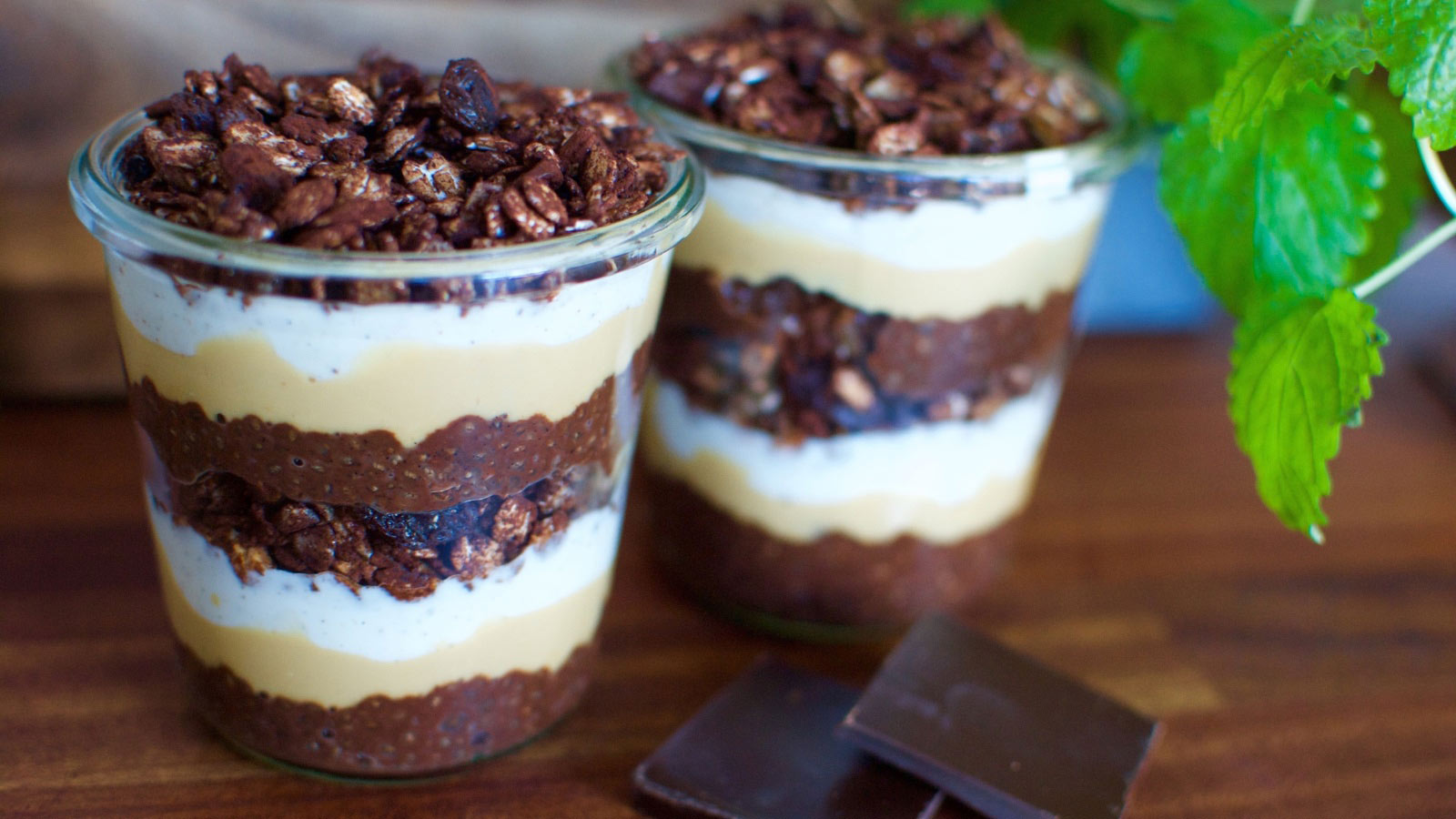 Chocolate peanut butter parfaits in two glass cups sitting on a wood surface.