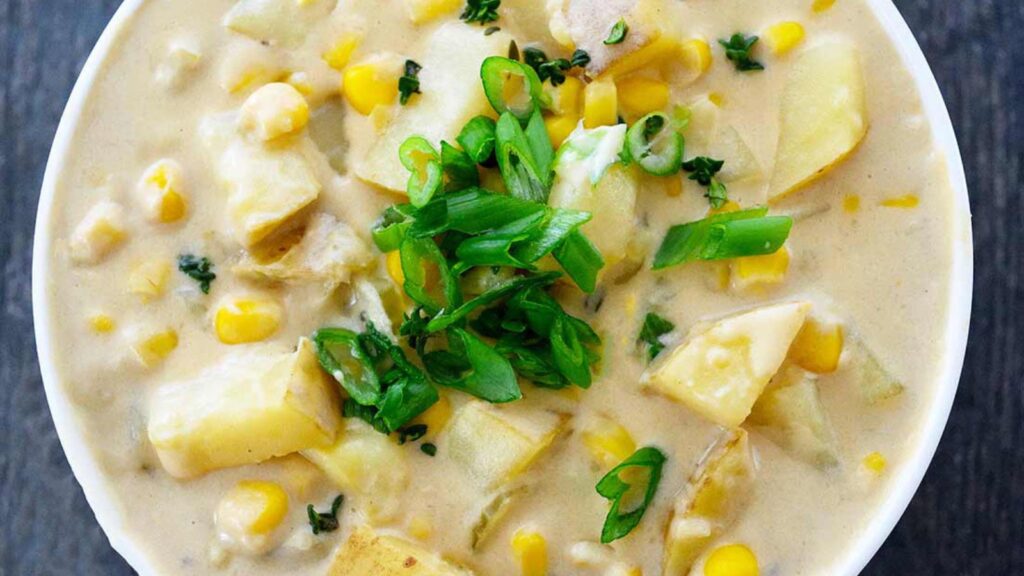 A white bowl filled with Potato Corn Chowder garnished with sliced green onions.