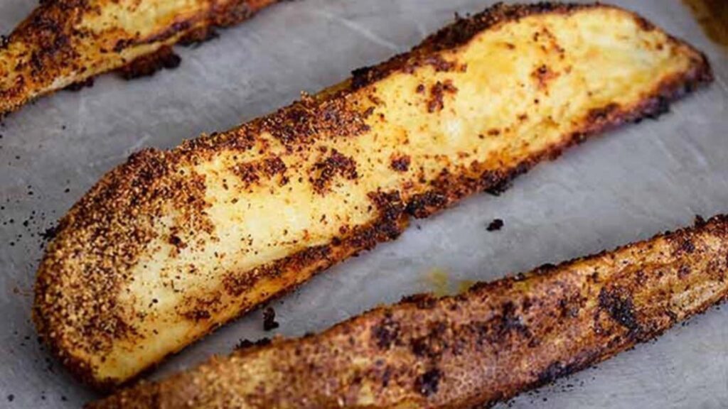 A few potato wedges laying on a parchment-lined baking sheet.