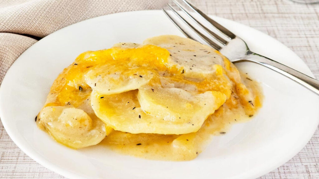 A serving of Potatoes Au Gratin on a white plate with a fork.