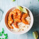 Overhead focus. White bowl filled with rice and topped with shrimp curry with lime wedges.