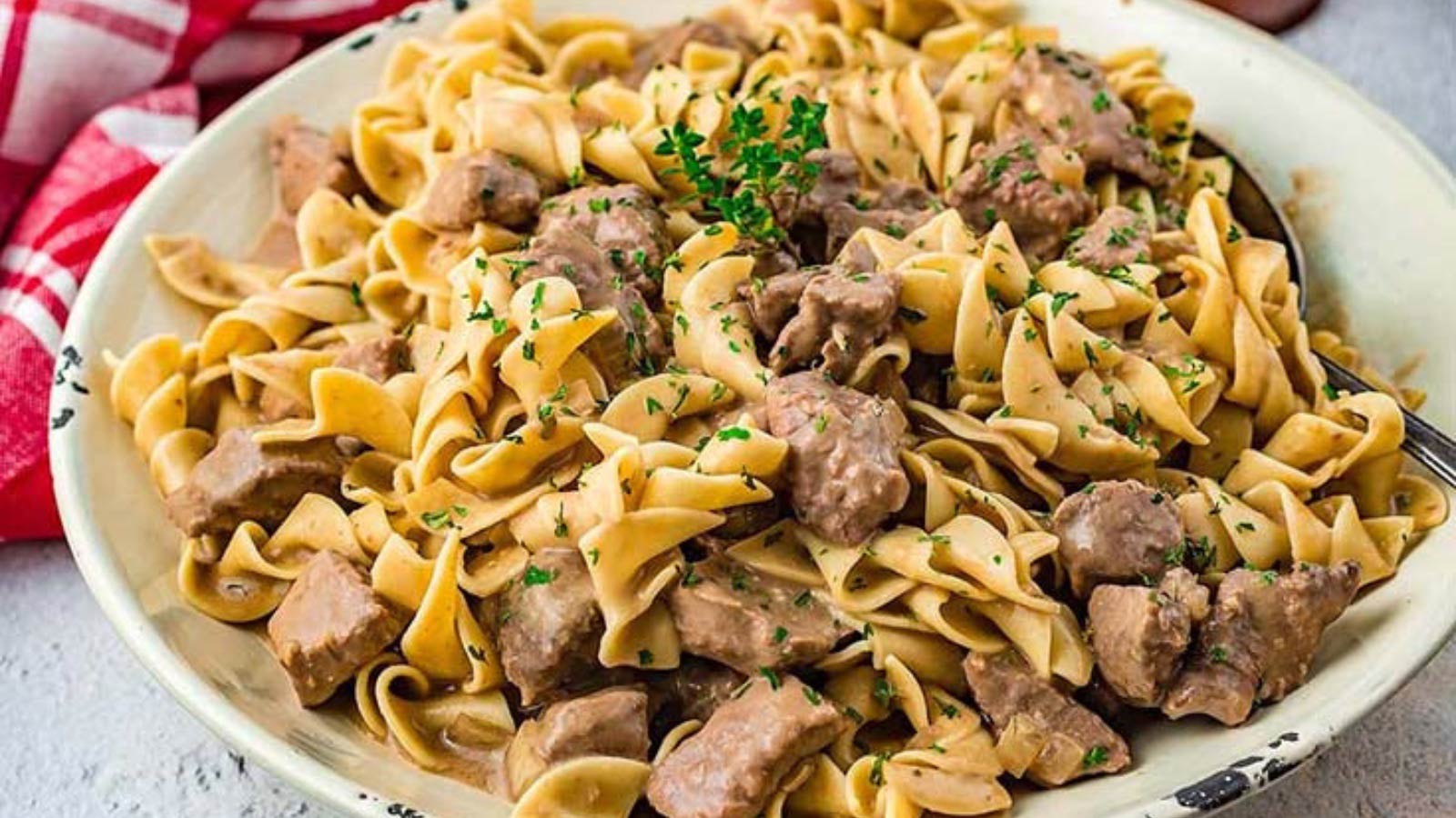 A white bowl on a table filled with slow cooker beef and noodles with mushrooms.