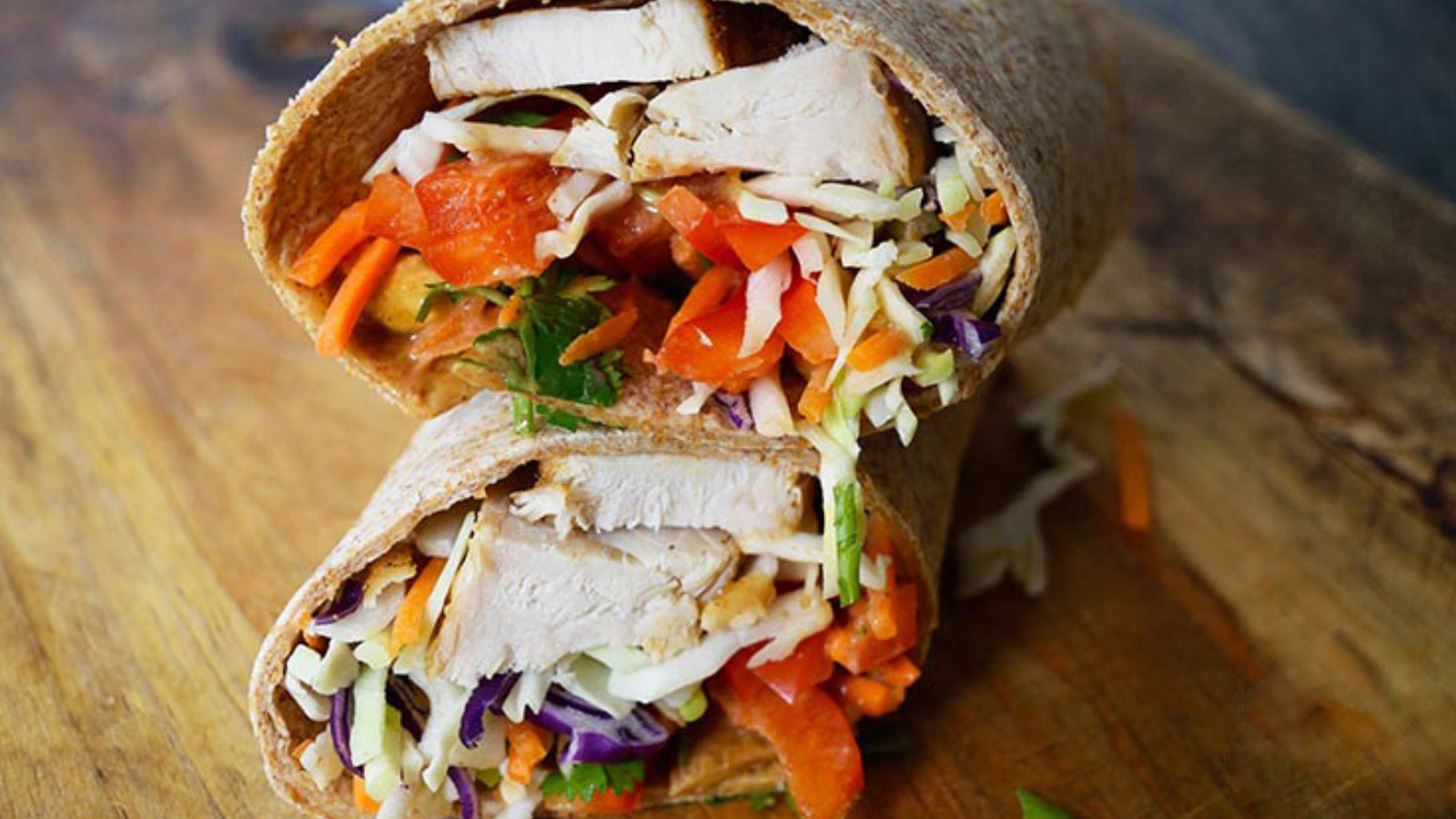 A finished Thai Peanut Chicken Wrap sitting on a cutting board.