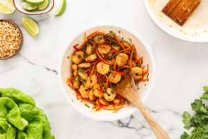 Shrimp added to fresh cut veggies in a white bowl.