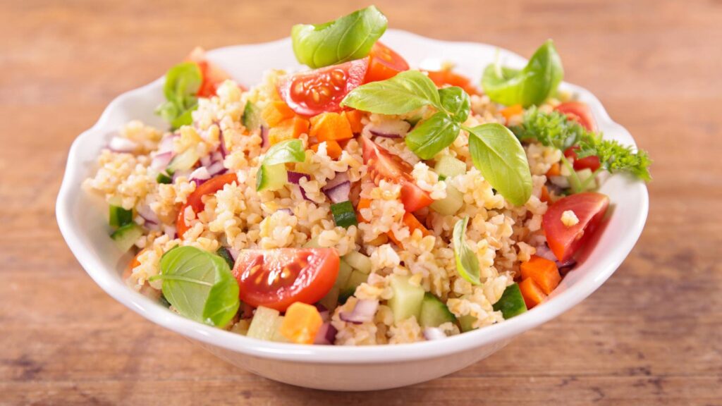 A white bowl filled with vegetable quinoa on a wood surface.