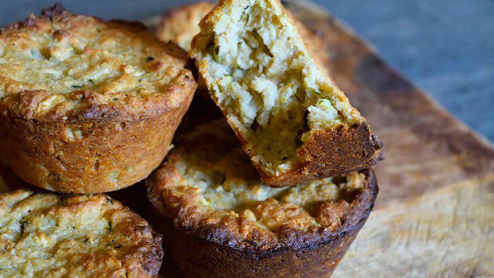 Several zucchini muffins on a cutting board. One has a bit removed.