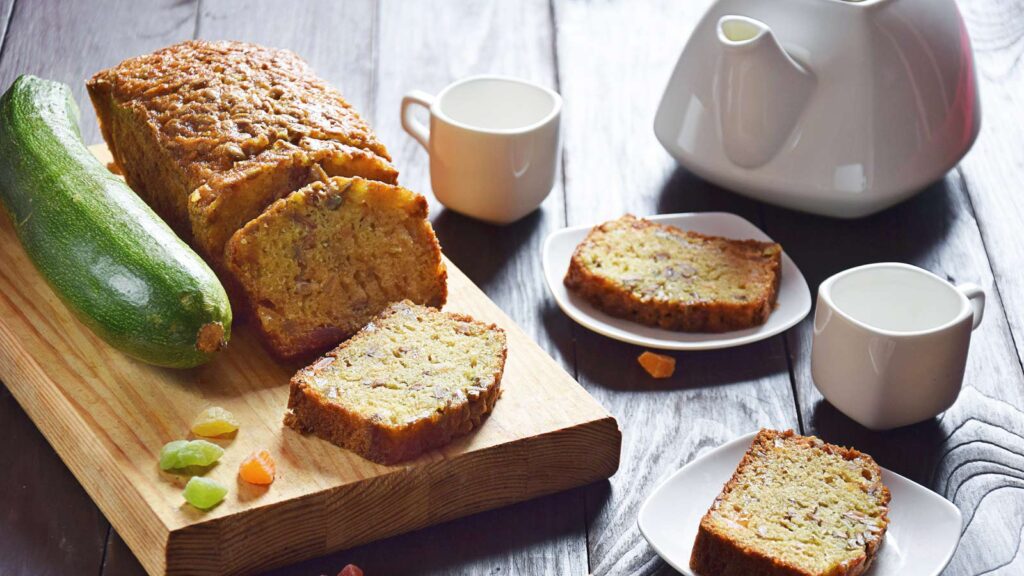 Delicious and fragrant zucchini bread sliced on a wood cutting board with a large zucchini laying next to it.