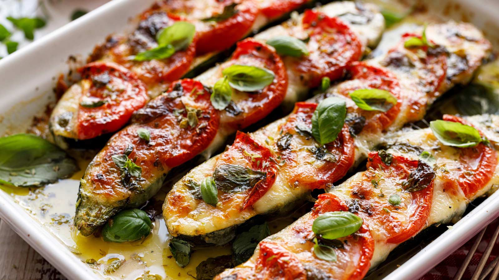 Roasted zucchini with the addition of tomatoes, mozzarella cheese, fresh basil and olive oil (caprese salad) in a ceramic baking dish, close-up.