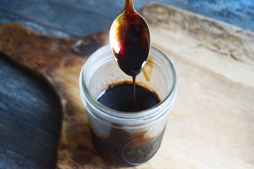 A spoon letting balsamic glaze drizzle off it into a jar.