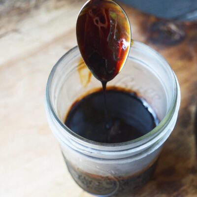 Drizzling balsamic glaze off a spoon into an open jar.
