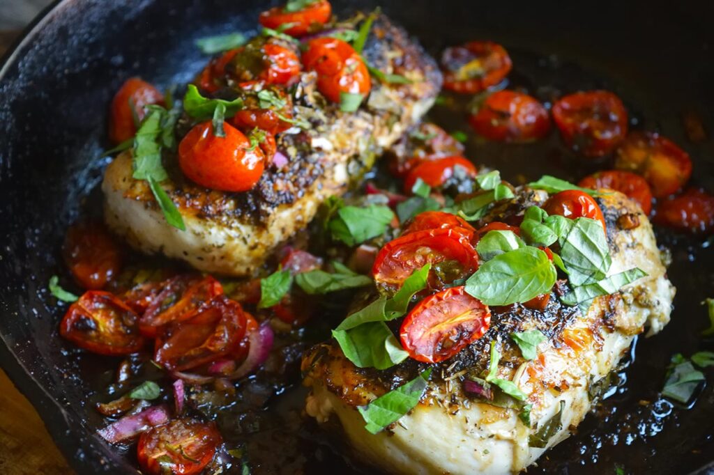 A closeup sideview of two pieces of bruschetta chicken in a skillet.