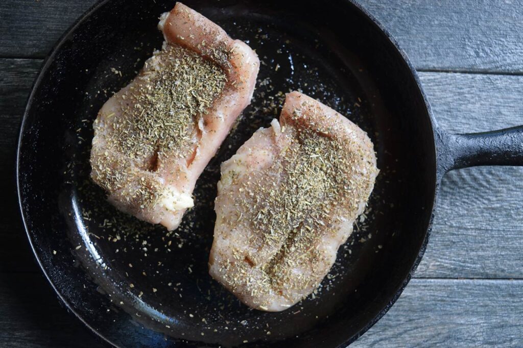 Two seasoned chicken breasts in a cast iron skillet.