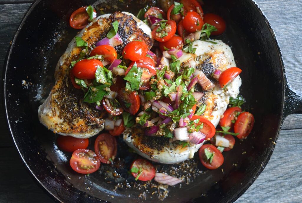 Seared chicken breasts with fresh bruschetta topping in a skillet.