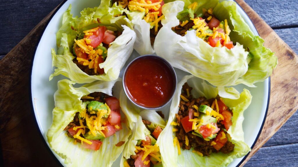 An overhead view of a round platter filled with California Lettuce Wraps with a small bowl of salsa in the middle.