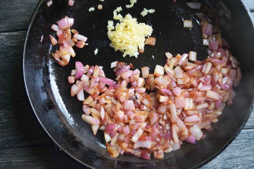 Adding fresh, pressed, garlic to a skillet with sautéd onions.
