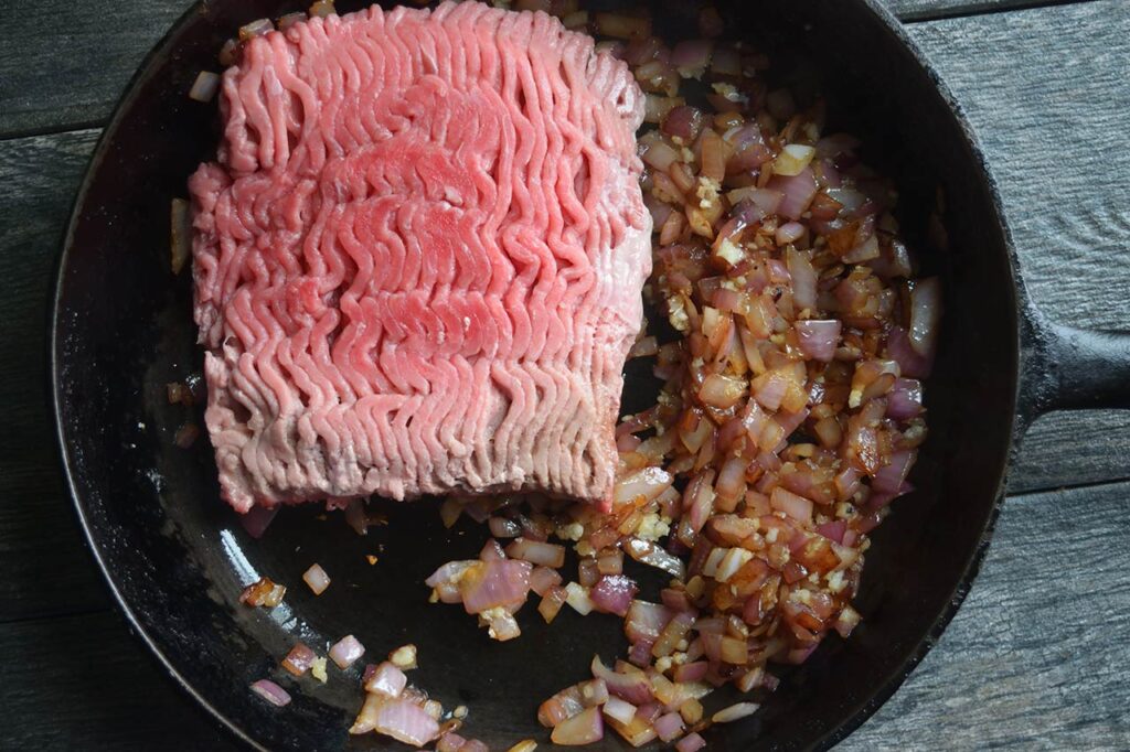 Raw ground turkey added to a skillet with sautéd onions and garlic.