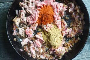 Spices added to a skillet filled with ground turkey, onions, and garlic.