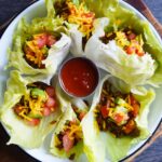 A white platter of Taco Lettuce Wraps sits on a wood cutting board on a slate surface.