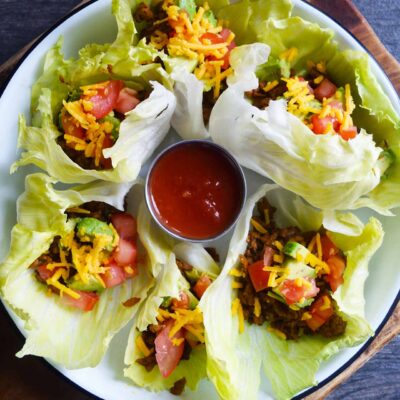 A white platter of Taco Lettuce Wraps sits on a wood cutting board on a slate surface.