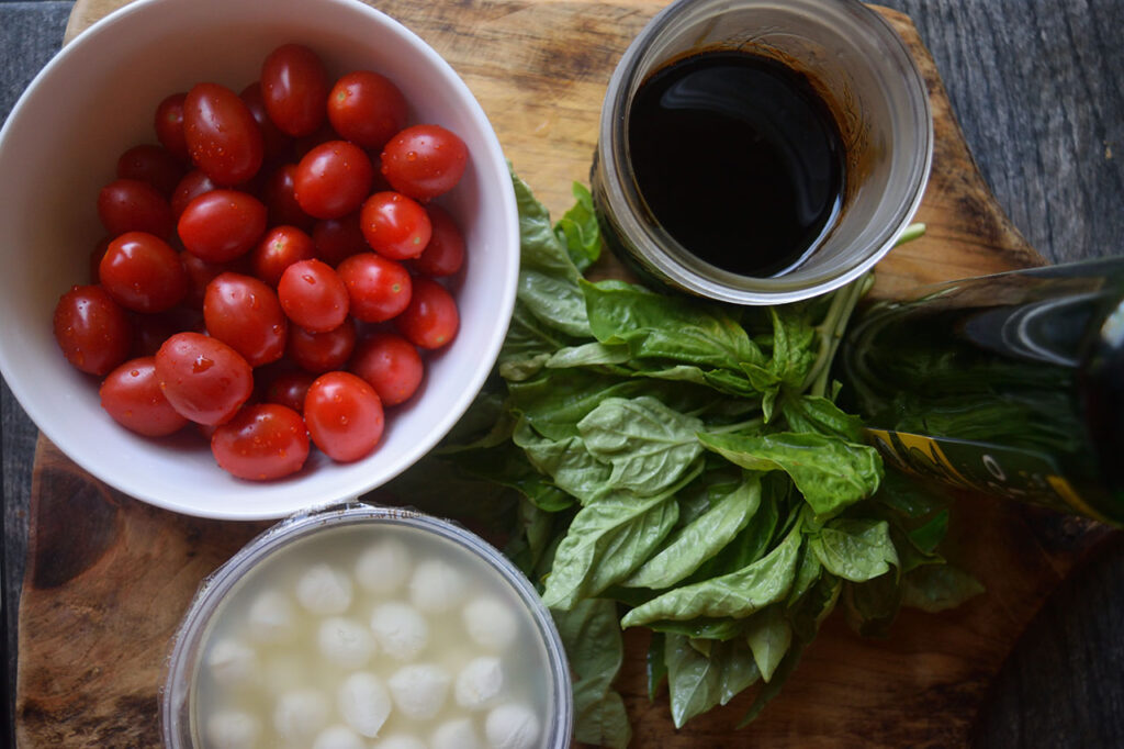 Caprese Skewers Recipe ingredients on a wood cutting board in individual containers.