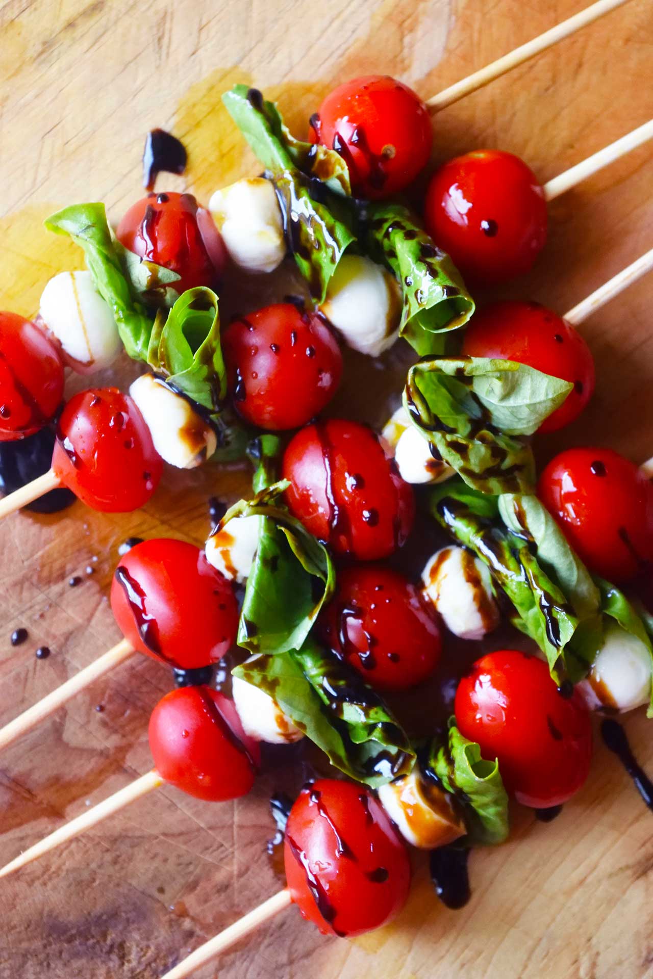 An overhead view of a row of Caprese Skewers drizzled with balsamic glaze.