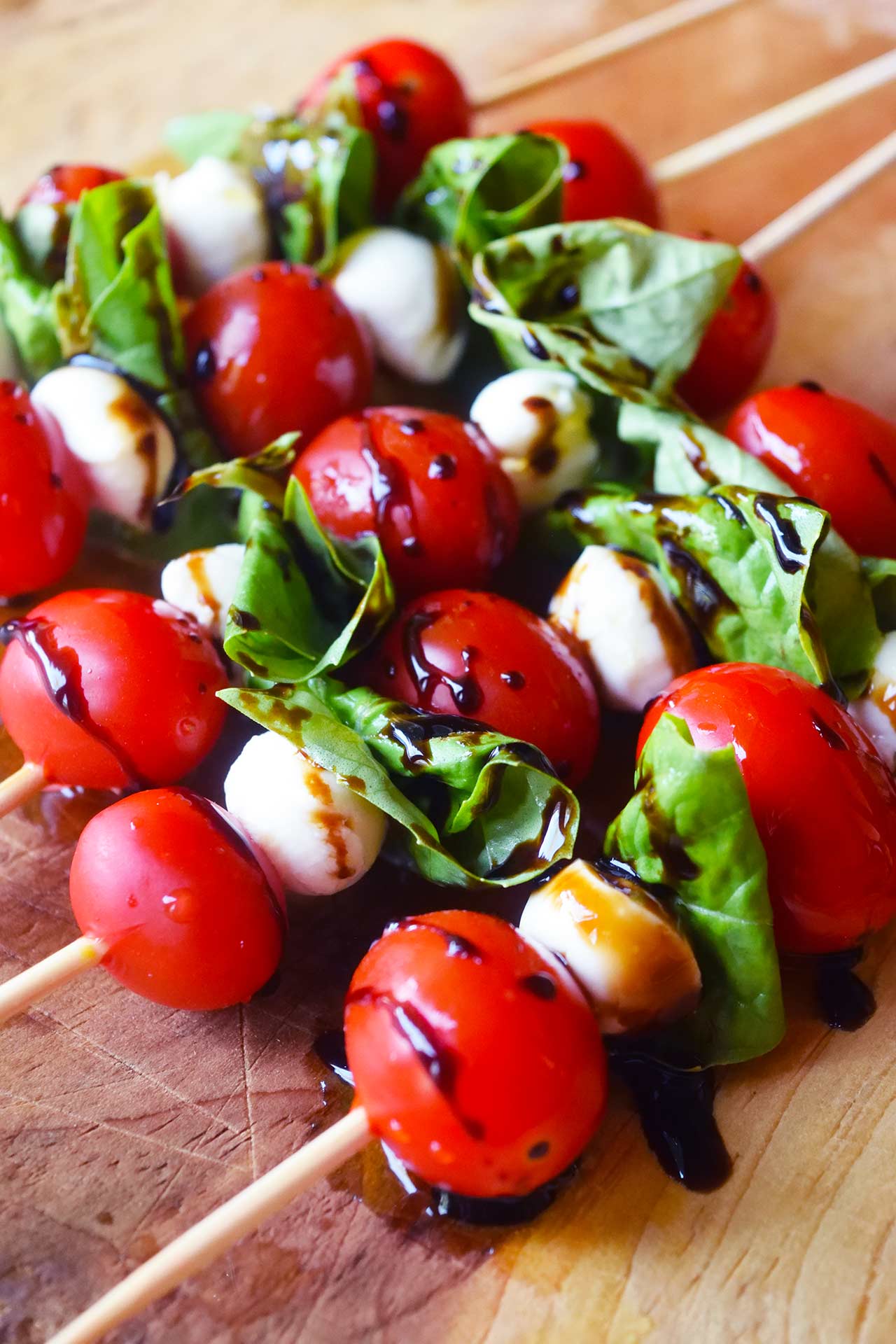 A side view of a row of Caprese Skewers on a wood cutting board.