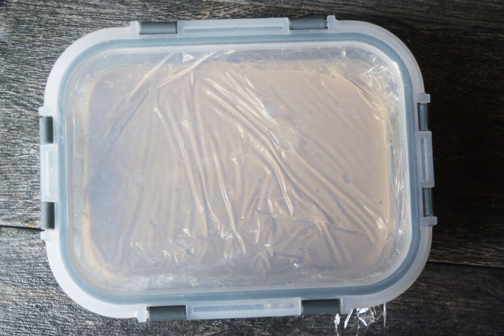 A lid placed of a plastic-wrapped container of coffee ice cream batter.