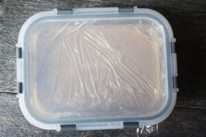 A lid placed of a plastic-wrapped container of coffee ice cream batter.