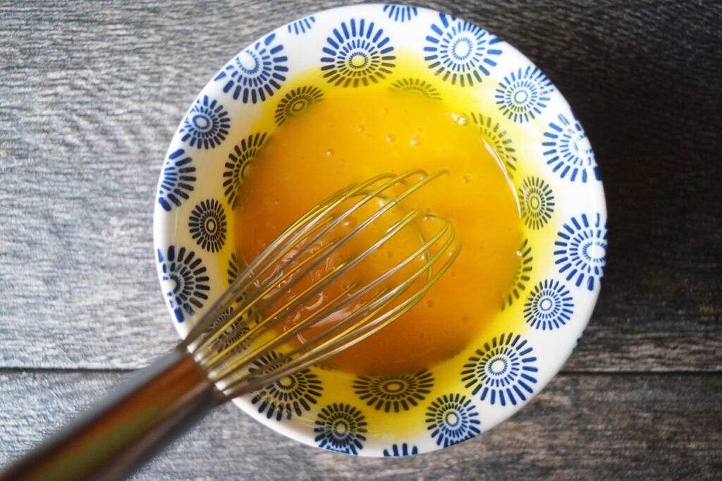 Whisked egg yolks in a small, decorative bowl with a whisk.