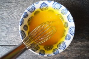 Whisked egg yolks in a small, decorative bowl with a whisk.