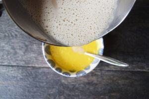 Pouring hot milk into a small bowl of egg yolks to temper them.