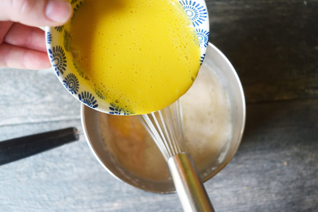 Pouring tempered egg yolks into hot honey oat milk in a pot.