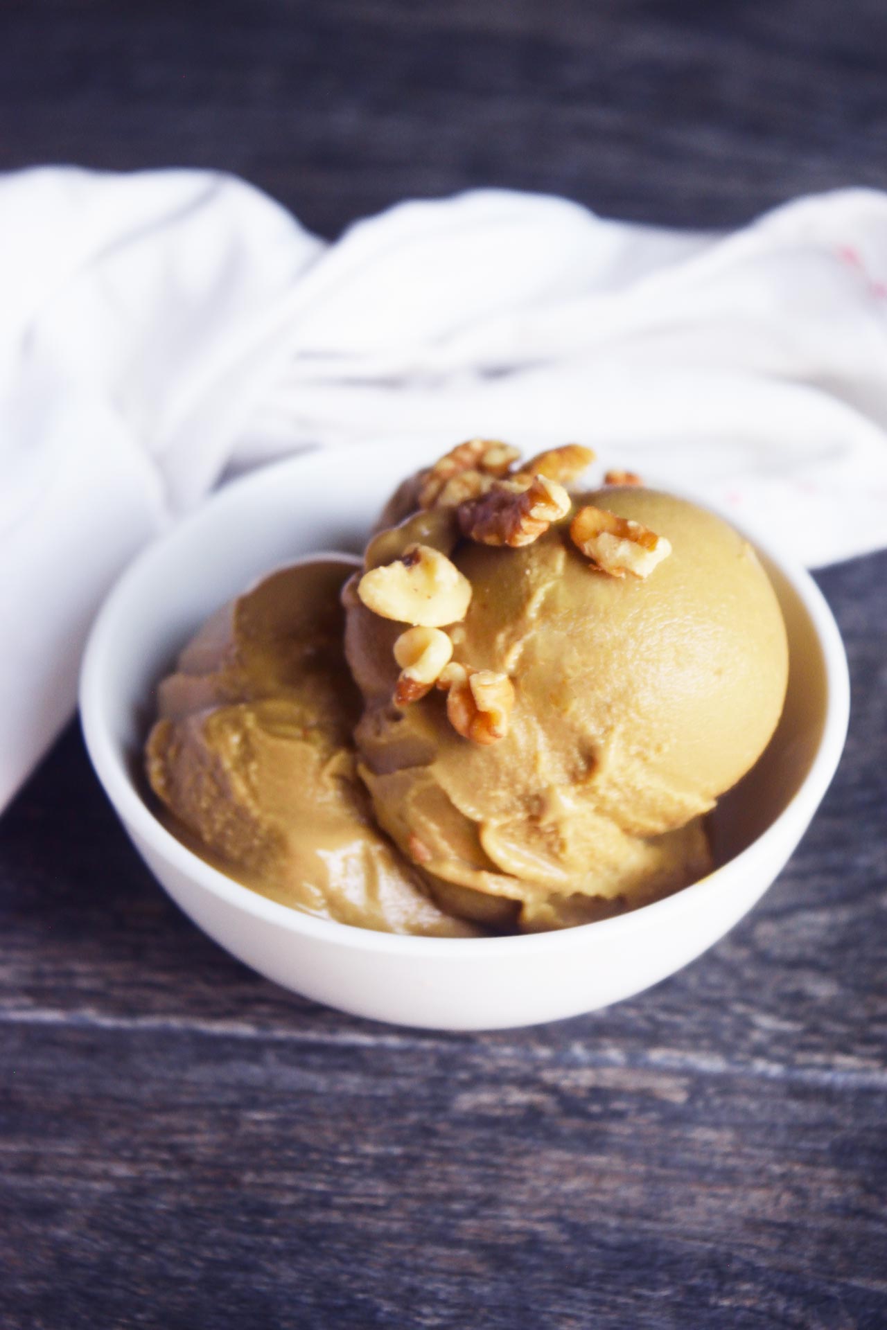 Scoops of coffee ice cream topped with walnut pieces in a white bowl.