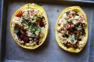 Baked spaghetti squash halves on a baking sheet garnished with fresh basil and balsmaic glaze.
